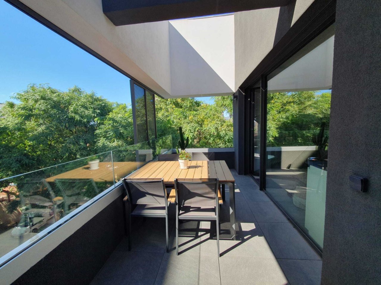 Moderne Terrasse mit durchdachtem Sonnenschutz und bodentiefen Glasschiebetüren zum Wohnbereich