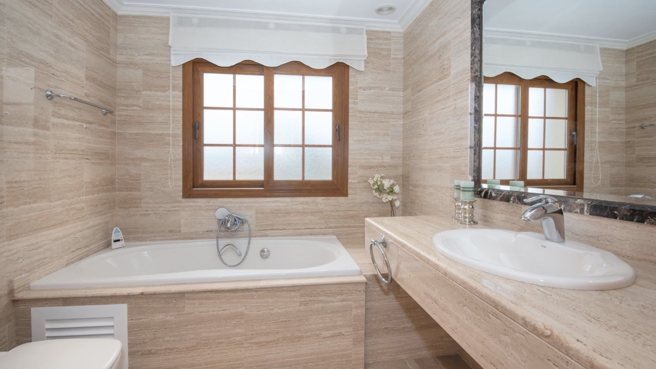 Exklusives Badezimmer mit Doppelwaschtisch, freistehender Badewanne und großflächigen Holzfenstern – Wellness auf höchstem Niveau