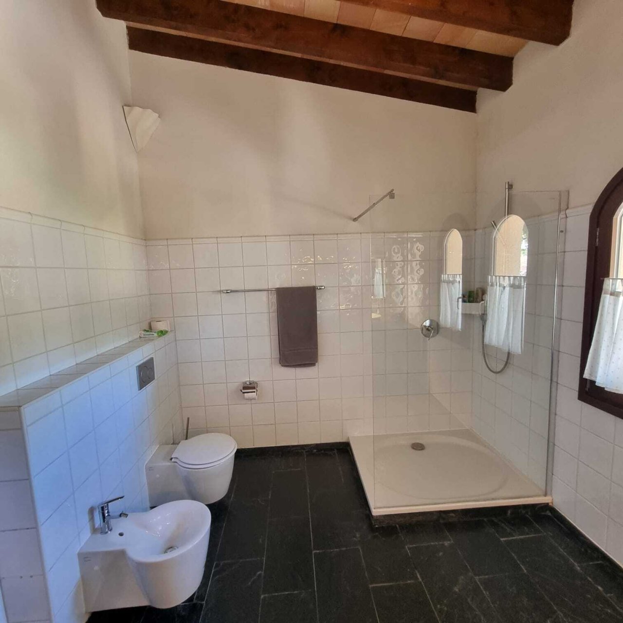 Modernes Badezimmer mit bodengleicher Dusche, Doppelwaschbecken und charaktervoller Holzbalkendecke Modernes Badezimmer mit bodengleicher Dusche, Doppelwaschbecken und charaktervoller Holzbalkendecke