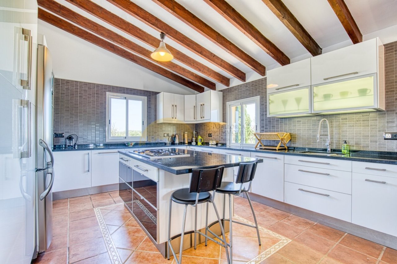 Moderne Küche mit Kochinsel, hochwertigen Arbeitsflächen und eleganten Deckenbalken