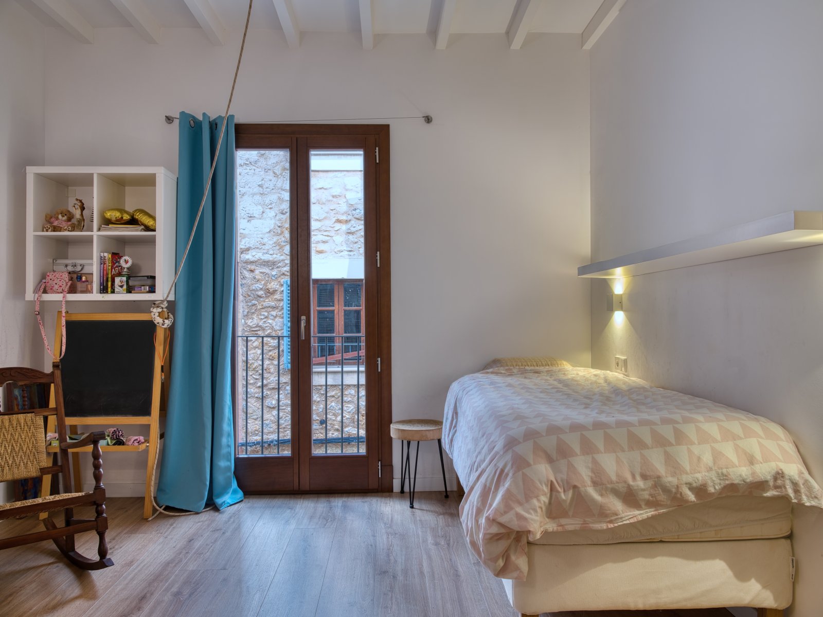 Bright bedroom with French balcony doors, exposed ceiling beams, and integrated wall lighting Bright bedroom with French balcony doors, exposed ceiling beams, and integrated wall lighting
