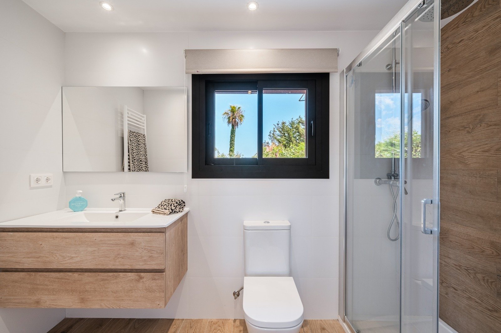 Modern bathroom with double sink, walk-in shower, and panoramic window with garden view