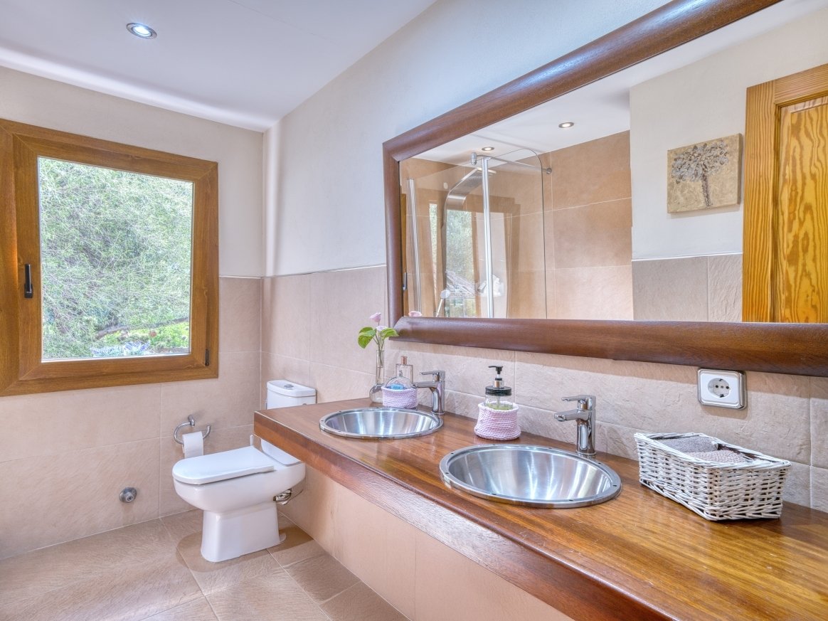 Elegant bathroom with double sink, walk-in shower, and window view of greenery