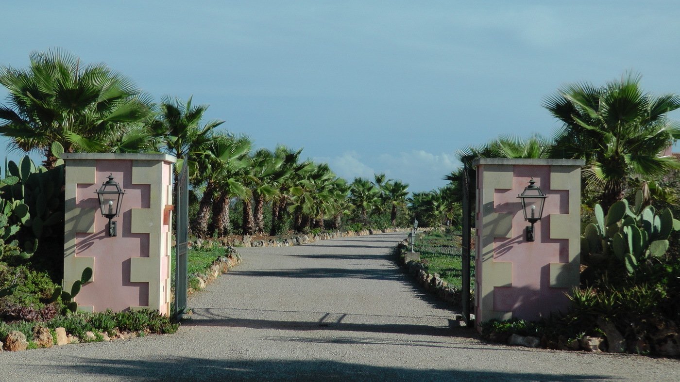 Imposing entrance gate with natural stone pillars and a palm-lined driveway
