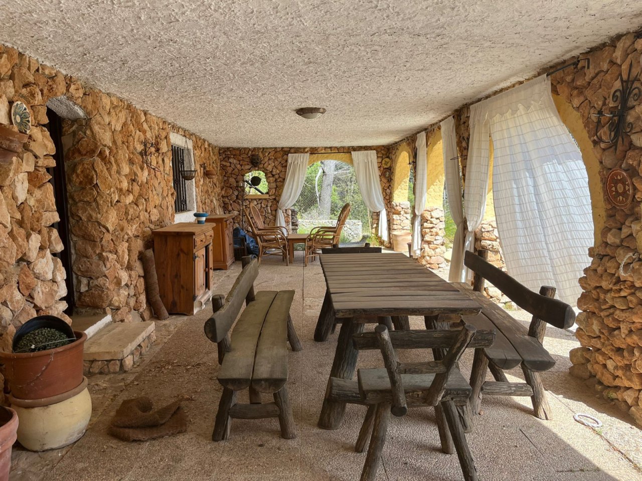 Covered lounge with natural stone walls – spacious dining area with direct garden view and rustic charm