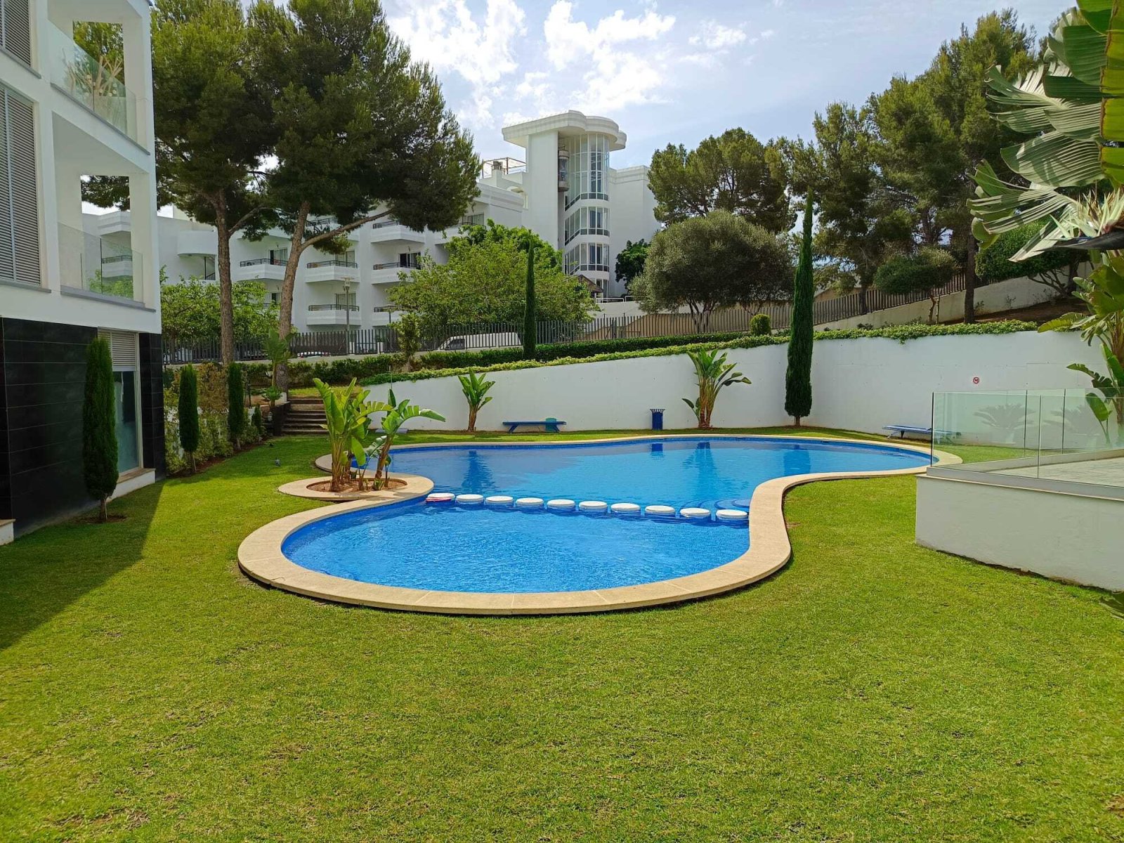 Pool facility with two pools, well-maintained lawn area, and secure glass enclosure Pool facility with two pools, well-maintained lawn area, and secure glass enclosure
