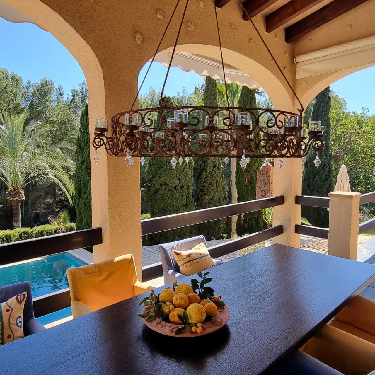 Covered terrace with wrought iron chandelier, pool view, and elegant column architecture Covered terrace with wrought iron chandelier, pool view, and elegant column architecture