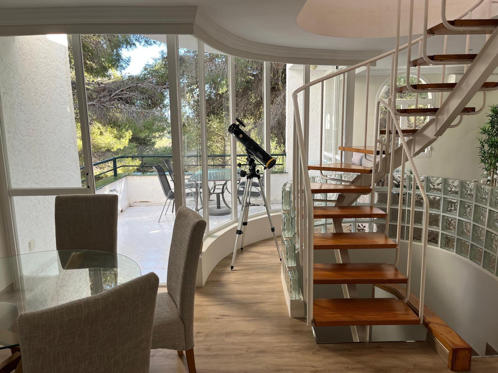 Área de estar llena de luz con elegante escalera en espiral y superficies de vidrio panorámicas hacia el exterior Área de estar llena de luz con elegante escalera en espiral y superficies de vidrio panorámicas hacia el exterior