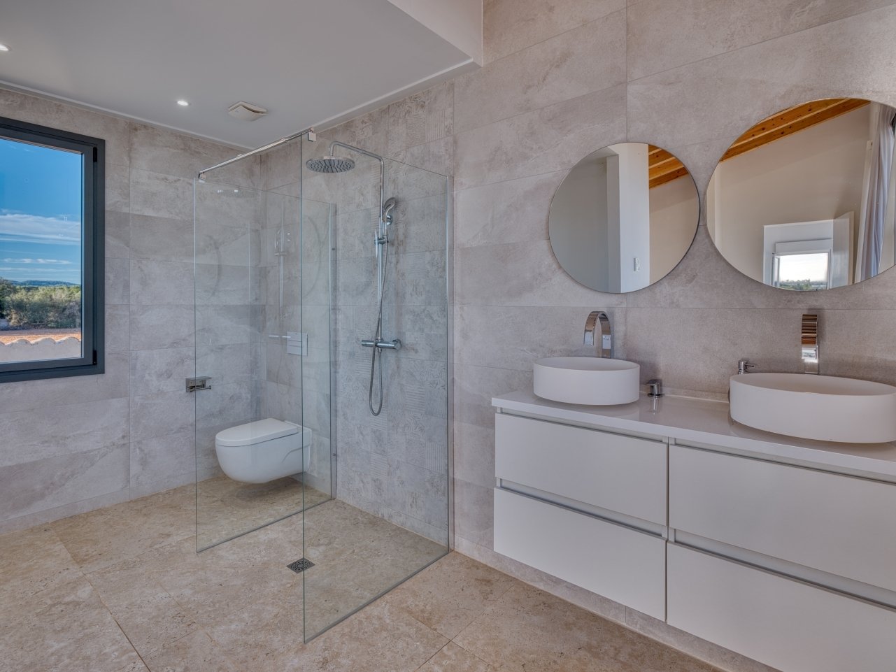 Baño moderno con ducha a nivel del suelo, doble lavabo y ventana panorámica con vista al paisaje