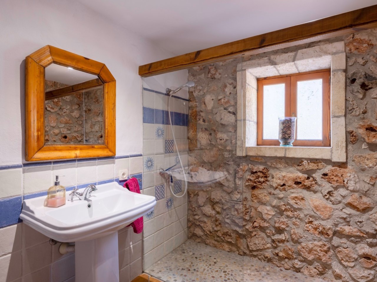 Baño con pared de piedra auténtica, ducha a nivel del suelo y viga de madera rústica