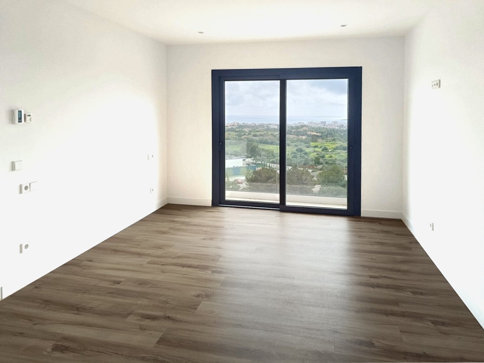 Habitación luminosa en esquina con puertas correderas de suelo a techo y vistas panorámicas del paisaje
