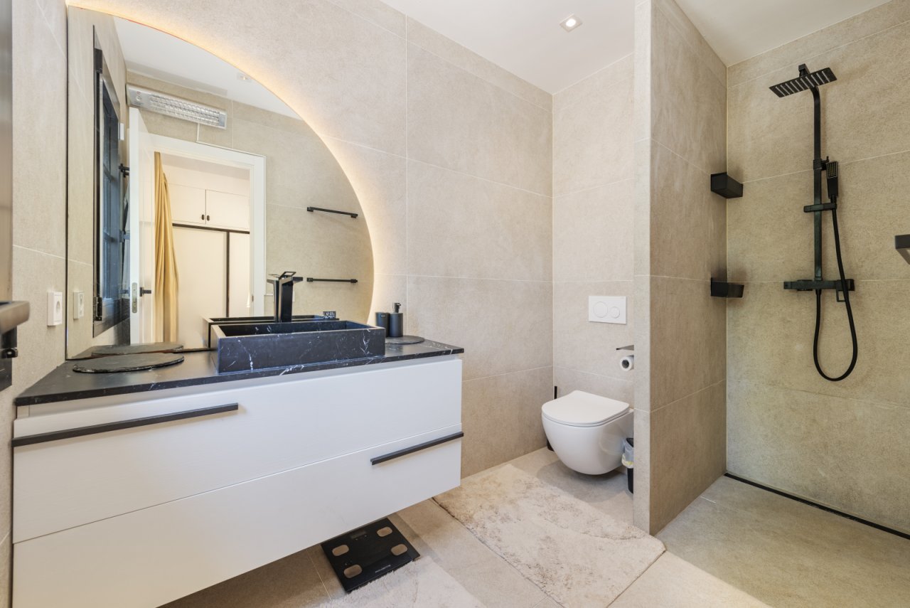 Baño moderno con ducha a ras de suelo, lavabo de mármol y distribución inteligente del espacio