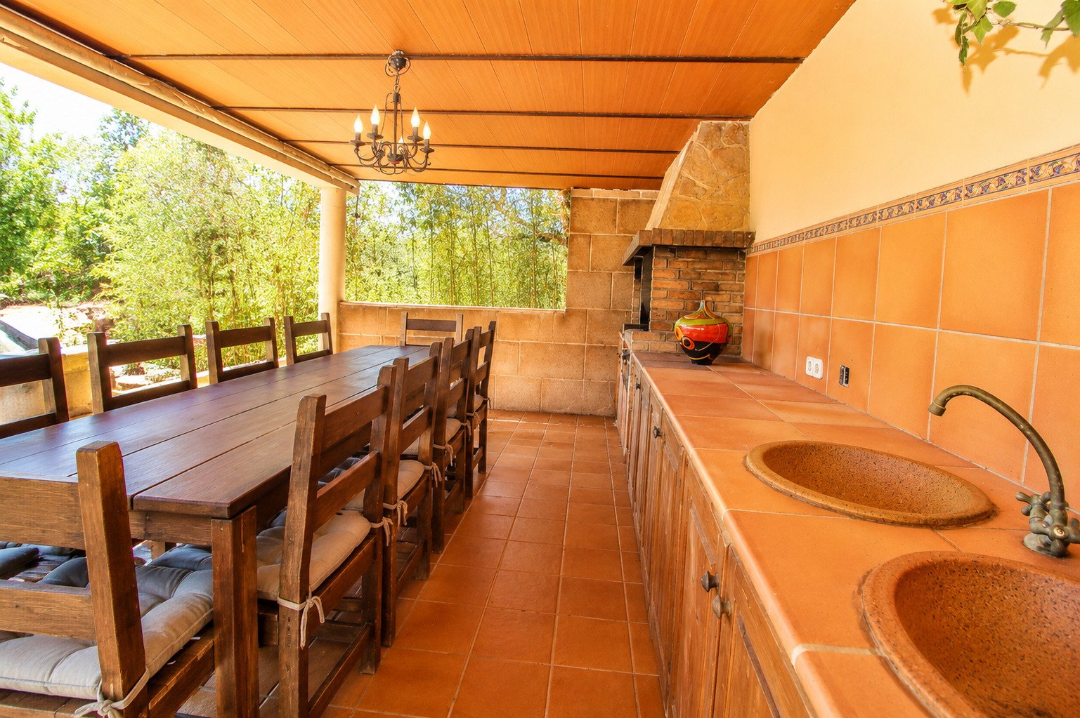 Cocina exterior cubierta con estufa de leña integrada y línea de visión abierta hacia la parcela forestal