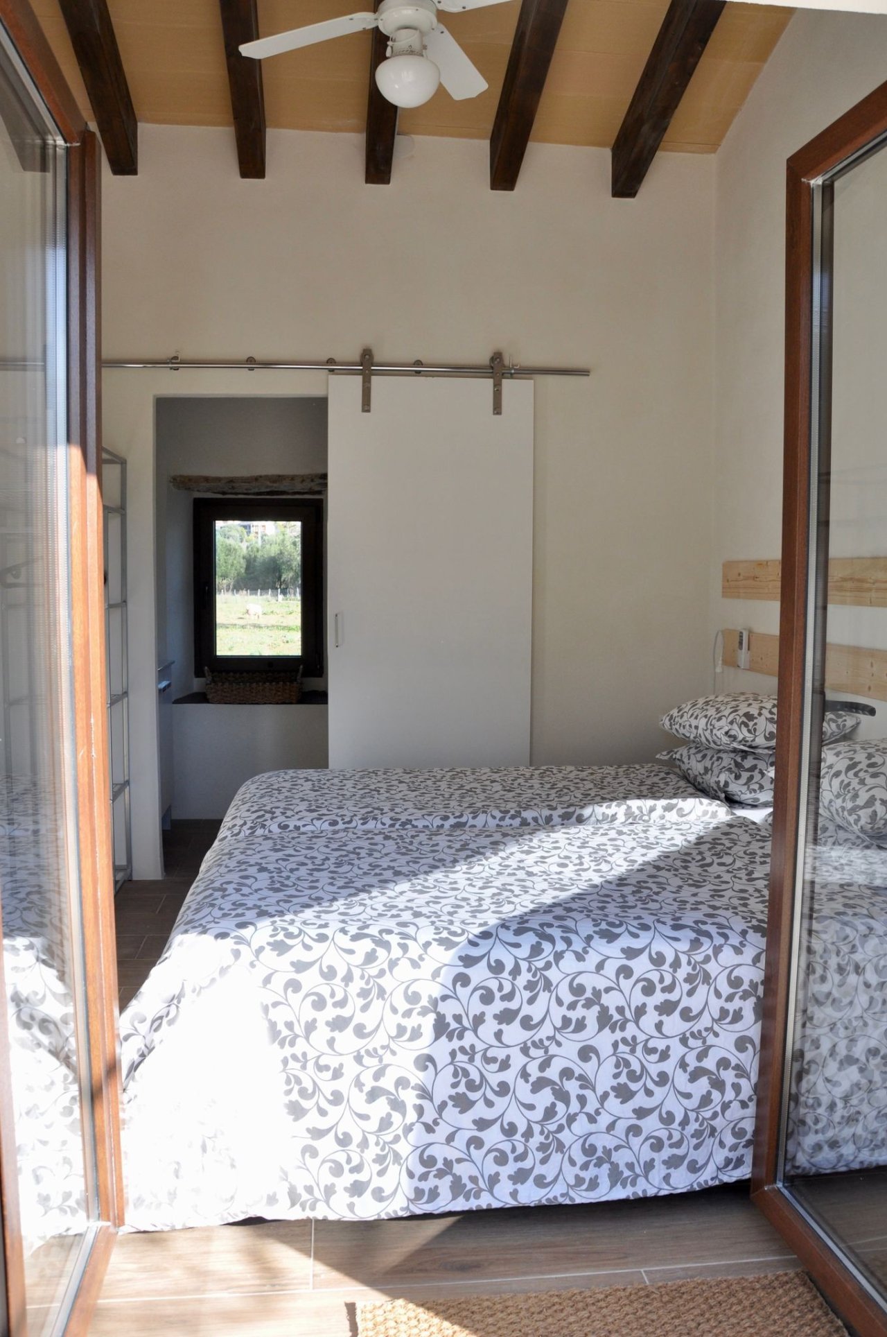Dormitorio con techo de vigas vistas y puerta corredera de suelo a techo hacia el baño adyacente