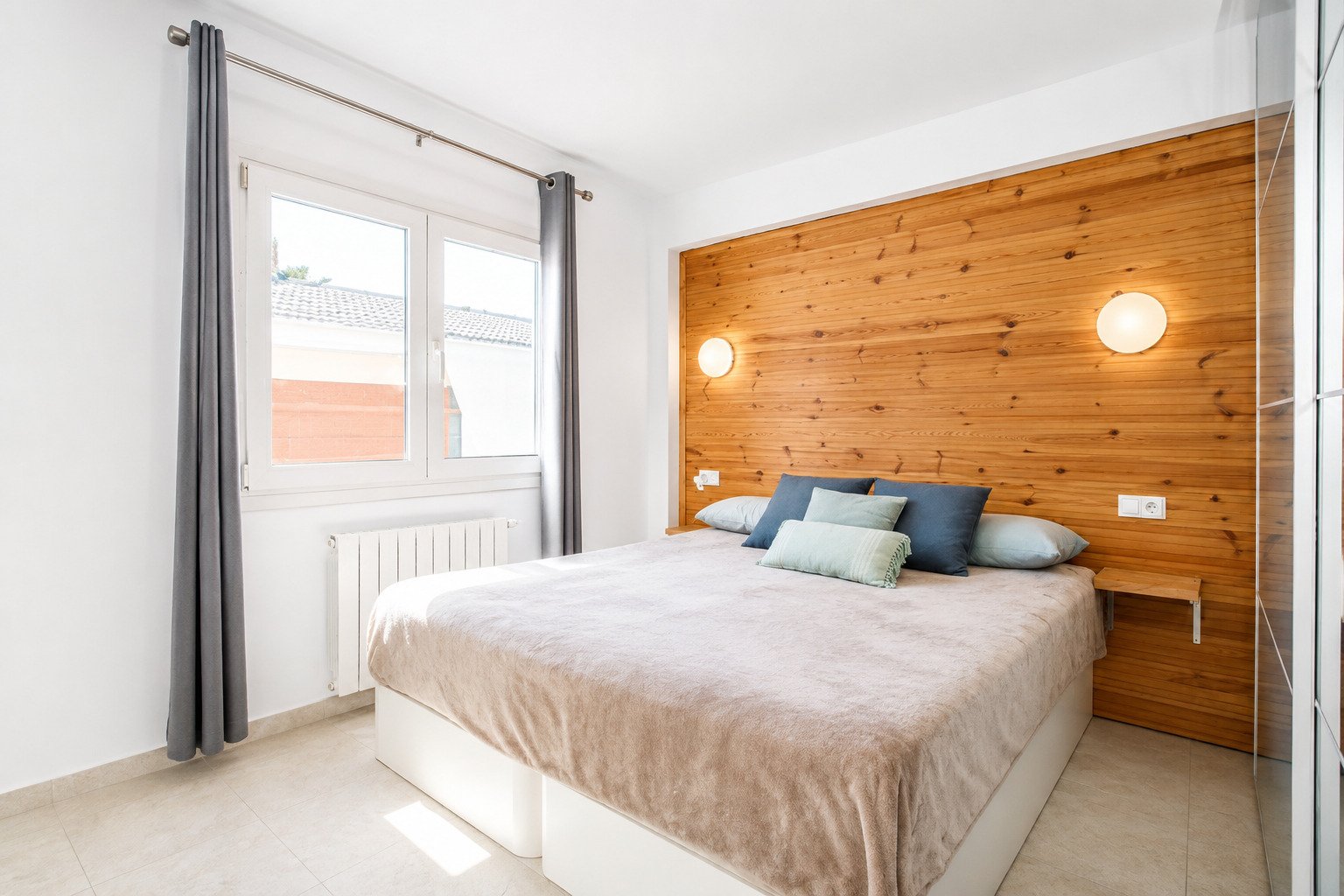 Dormitorio luminoso con pared de acento de madera y amplias ventanas.