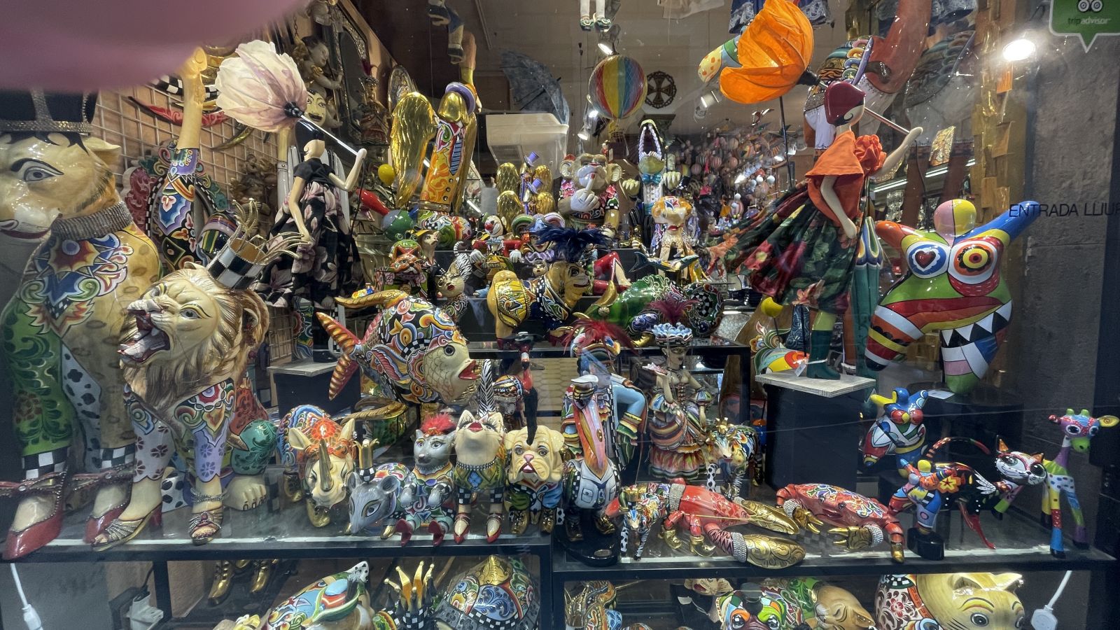 Zwei Schaufenster mit bunten, kunstvollen Gesichtern und Skulpturen in einer Seitenstraße Barcelonas.
