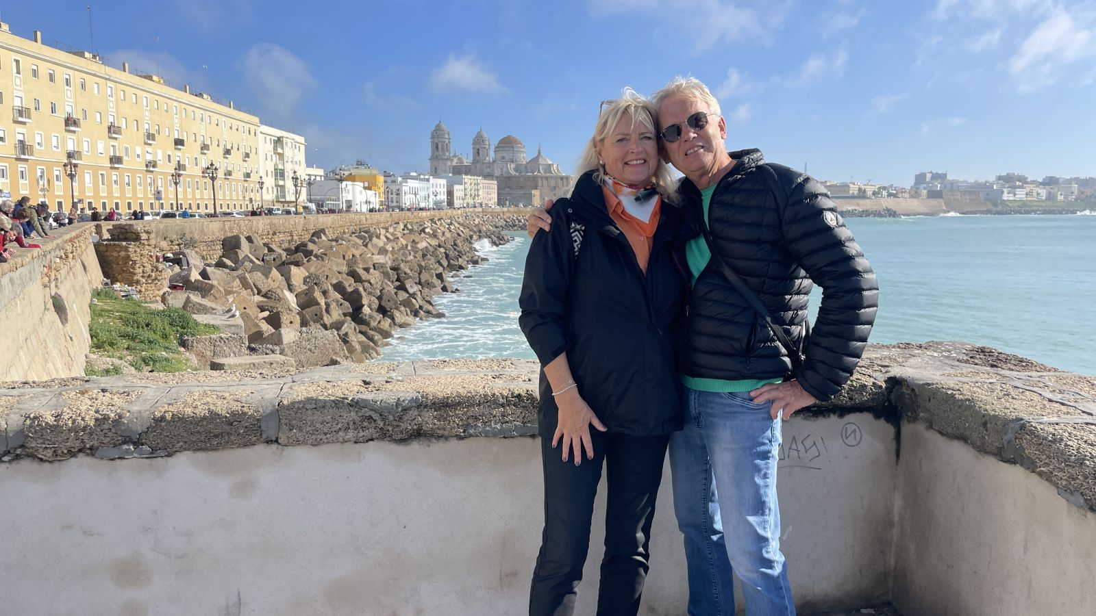 laudia und Axel stehen vor dem tiefblauen Atlantik an der Promenade von Cádiz.