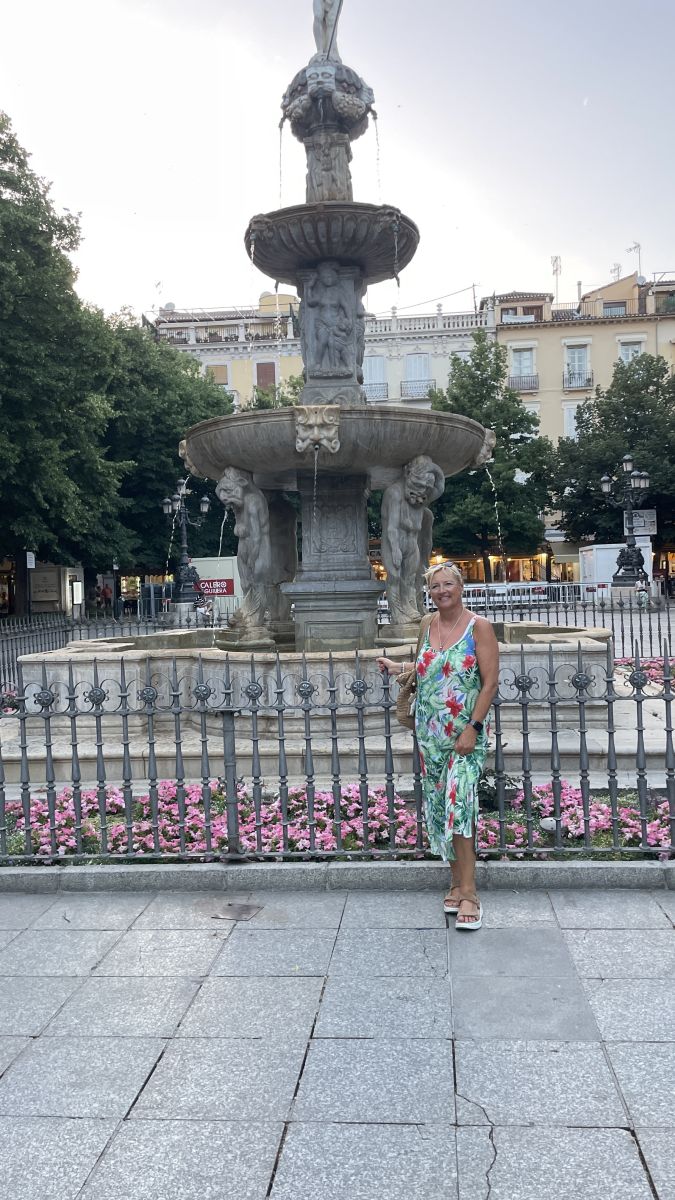 Steinerner Stadtbrunnen in der Altstadt von Granada mit Blumen und Passanten