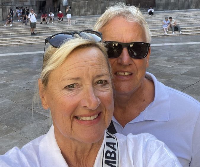 „Zwei Personen stehen entspannt vor einem historischen Gebäude auf Mallorca an einem sonnigen Oktobertag. Im Hintergrund leuchtet der blaue Himmel – das milde Wetter im Herbst lädt zum Entdecken der Insel ein.“
