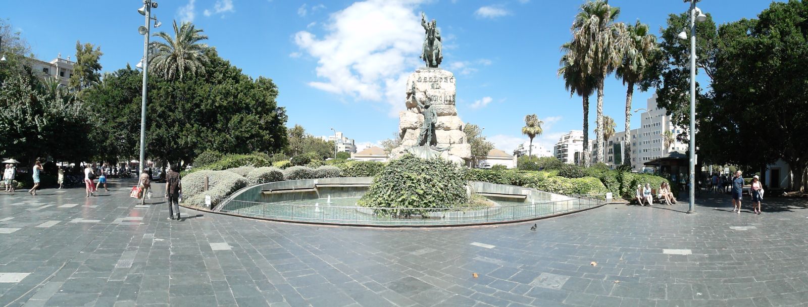 Panoramaaufnahme des Plaza España in Palma de Mallorca mit Blick auf die Reiterstatue von König Jaime I., umliegende Bäume, Cafés und den zentralen Busbahnhof im Hintergrund bei sonnigem Oktoberwetter.
