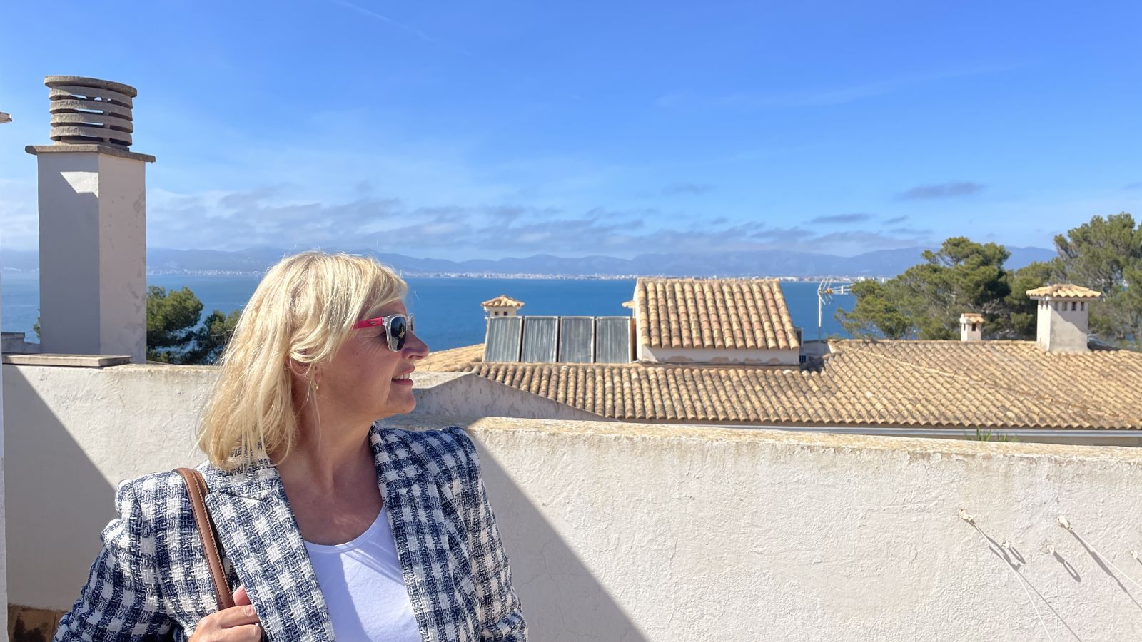 Claudia sitzt auf einer Terrasse mit Blick auf die mallorquinische Landschaft, umgeben von blauem Himmel und Sonne – typisch für das milde und freundliche Wetter auf Mallorca im Oktober.