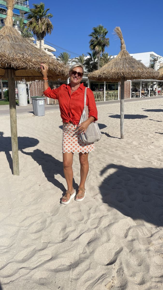 Claudia genießt die Sonne am weißen Sandstrand von Mallorca, mit Blick auf das türkisfarbene Meer.