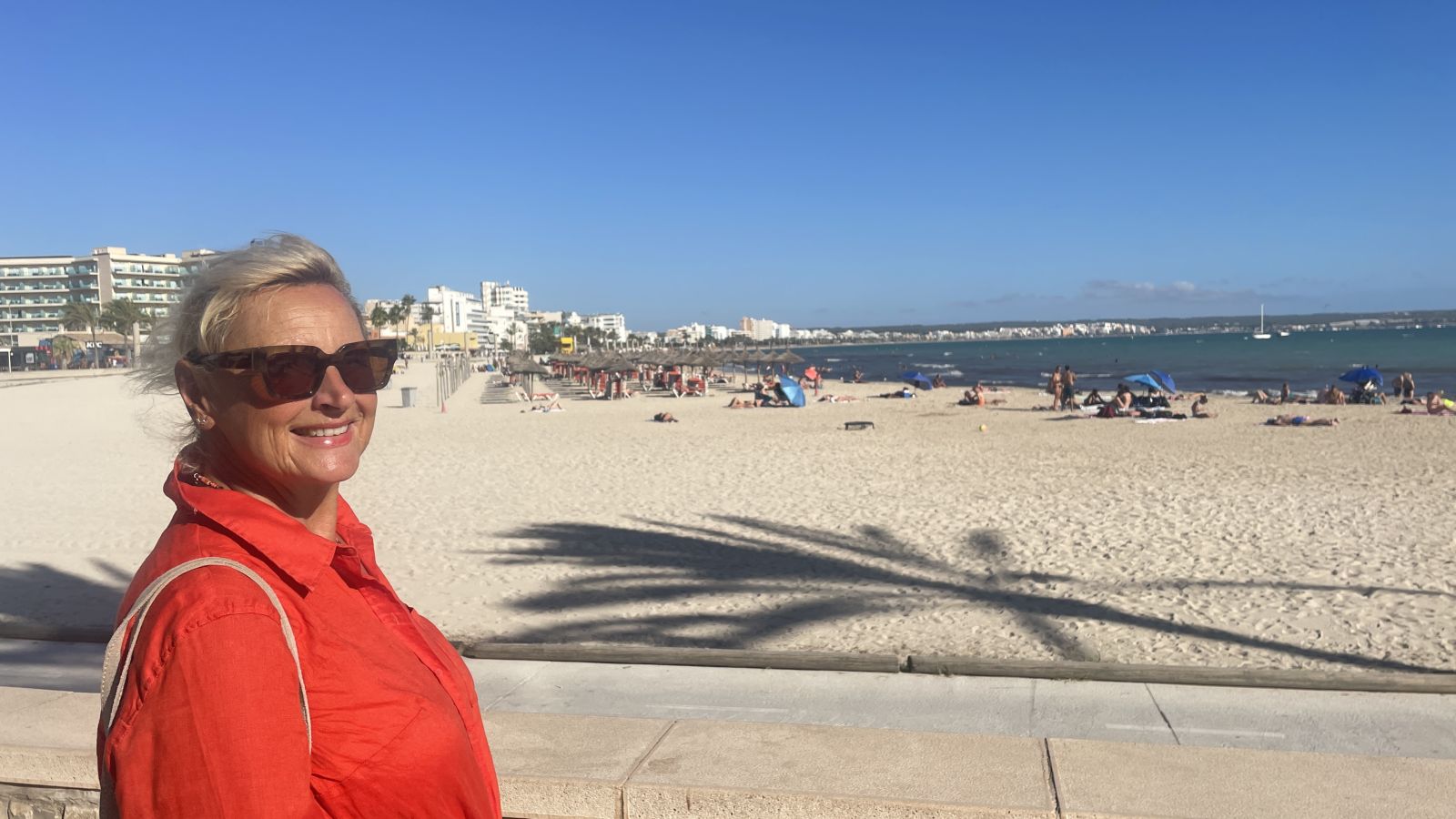 Claudia am Sandstrand von Mallorca, umgeben von Meer und blauem Himmel.